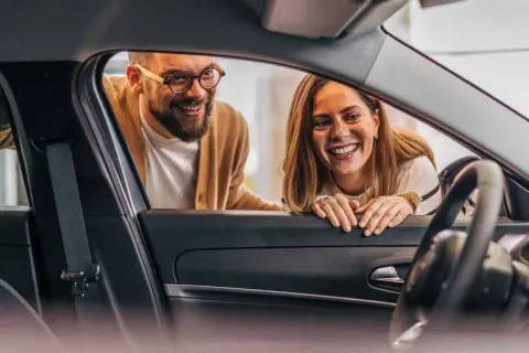 Ett leende par tittar in i en ny bil. De funderar på hur funkar privatleasing för att få sin drömbil.