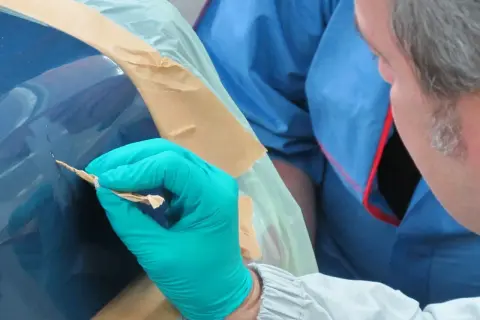 Mann mit Handschuh entfernt Rost von Autolack. Sorgfältige Arbeit, um das Auto entrosten.