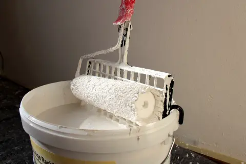 Farbroller mit Silikatfarbe in einem Eimer. Die Nachteile von Silikatfarbe sind die schwierige Verarbeitung und die geringe Farbtonauswahl.