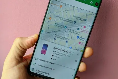 Mano sujetando un móvil que muestra la función de localizar móvil. Se ve un mapa de la Ciudad de México y opciones para reproducir sonido o proteger el dispositivo.