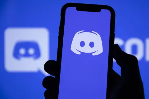 Dłoń trzyma smartfon z logo Discord. Aplikacja ta służy do komunikacji, więc jeśli zastanawiasz się "discord co to", to właśnie ją widzisz.