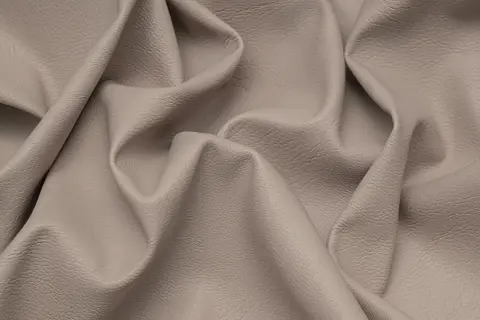 Miękka, beżowa eko skóra z delikatną fakturą, pofałdowana tworząc eleganckie draperie.