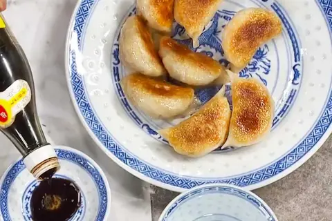 Stekta vegetariska dumplings serveras på en blåvit tallrik. Sojasås hälls upp i en liten skål. Ett perfekt vegetariska dumplings recept!