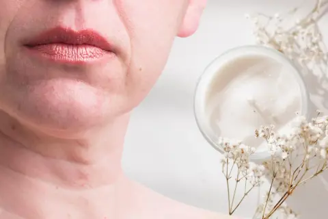 Un vasetto di crema e fiori secchi accanto al viso di una donna, suggerendo come migliorare la pelle del viso con prodotti naturali.