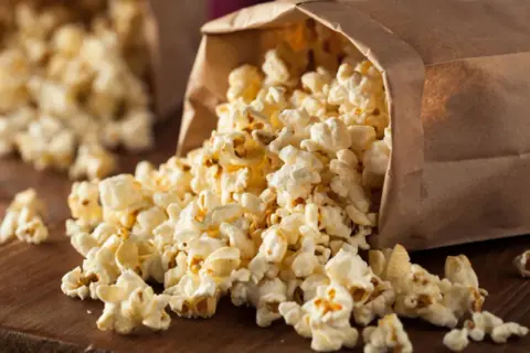 Frischer Popcorn fließt aus einer Papiertüte. Perfekt für kalorienarme Snacks beim Filmabend.