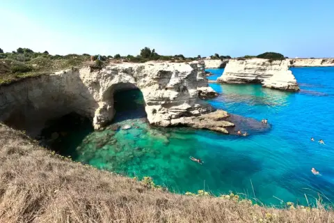 Scogliere bianche e mare cristallino nel Salento, con persone che nuotano e si godono il sole.
