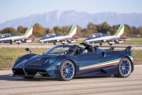 Niebieski Pagani Huayra Roadster z włoską flagą na boku, obok samolotów akrobacyjnych. Jego pagani huayra cena jest astronomiczna.