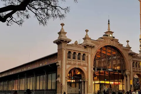 El **mercado central Zaragoza** con su arquitectura de hierro y cristal, iluminado al atardecer. Gente pasea por la entrada principal.