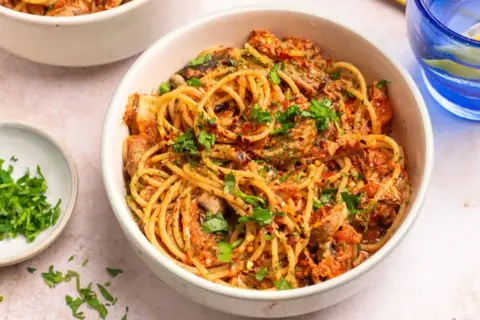 Miseczka spaghetti z sosem pomidorowym, grzybami i posiekaną natką pietruszki.