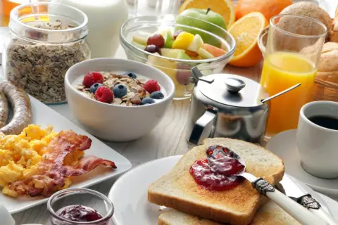 Ein reichhaltiges Frühstück in Görlitz: Rührei, Speck, Würstchen, Müsli, Obst, Toast mit Marmelade, Saft und Kaffee.