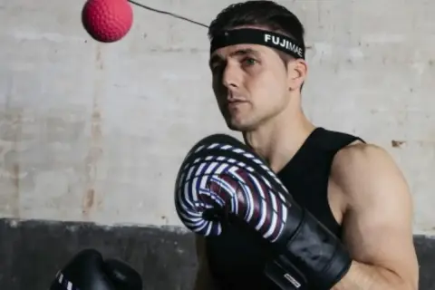 Bokser w rękawicach i opasce FUJIMAE, japoński producent sprzętu sportowego, ćwiczy z piłką refleksyjną.