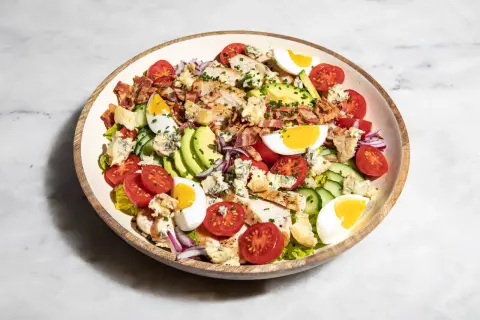 Ein üppiger Cobb Salad deutsch mit Hähnchen, Speck, Ei, Avocado, Tomaten und Blauschimmelkäse.