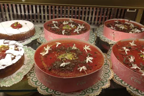 Deliziosi dolci in vetrina, tra cui un tortino con zucchero a velo e un invitante gelo di anguria decorato con fiori bianchi e scaglie di cioccolato.