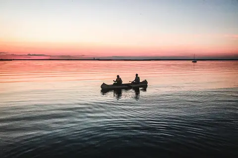 Två personer paddlar kanot i solnedgången. En perfekt plats att fundera på vart ska man resa i juli.