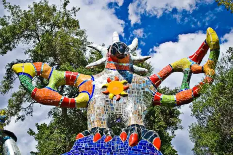 La scultura colorata del Giardino dei Tarocchi in Toscana, con il suo sole radioso e le braccia aperte, sembra accogliere i visitatori in un mondo magico.