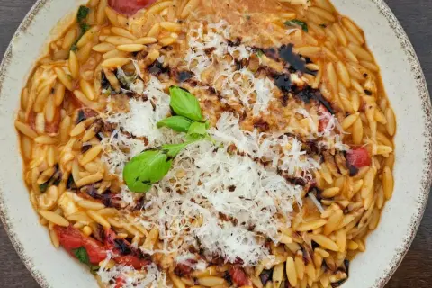 Ein Teller mit cremigen Orzo Nudeln, garniert mit geriebenem Parmesan, frischem Basilikum und Balsamico-Glasur.
