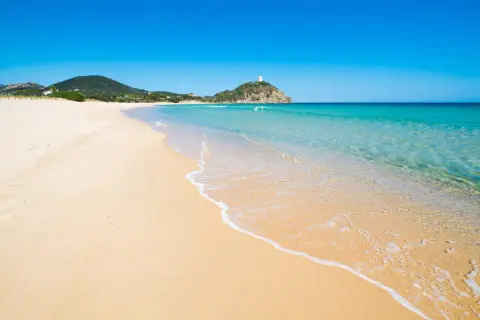 Piękne plaże Cagliari z turkusową wodą i złotym piaskiem. W oddali widać wzgórze z wieżą.