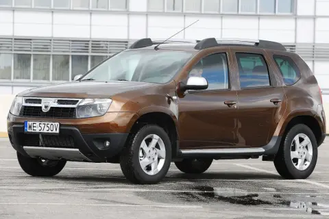 Brązowy Dacia Duster na parkingu, gotowy do testu. Widoczny kierowca za kierownicą.