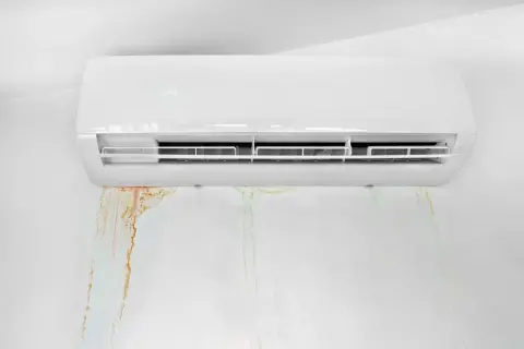 Condizionatore che perde acqua, lasciando macchie umide e colorate sul muro bianco.