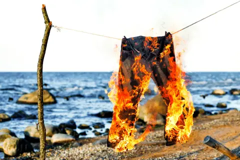 Jeans brennen am Strand, ein Symbol für den Polterabend. Die Flammen tanzen, während die Wellen rauschen.