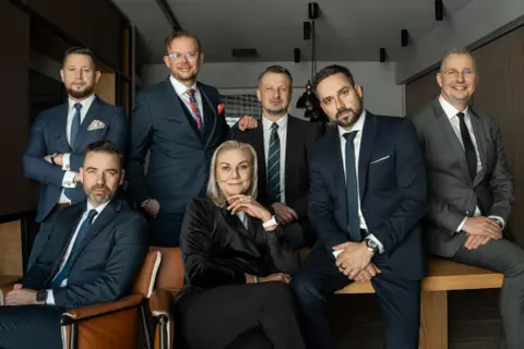 Grupa siedmiu profesjonalistów w garniturach, pozujących do zdjęcia w nowoczesnym biurze.
