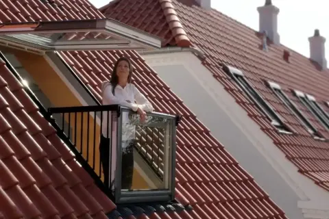 Kobieta na balkonie wychodzącym z okienka w dachu, podziwia widok.