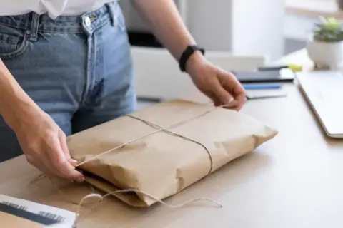 Ręce wiążą sznurkiem paczkę owiniętą w papier. Gdzie nadać mini paczkę Poczta Polska?