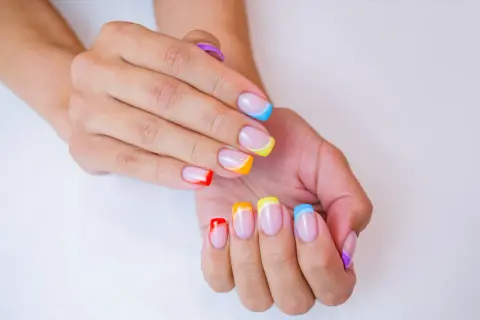 Kolorowe paznokcie na lato: francuski manicure w odcieniach tęczy, od czerwieni po fiolet.