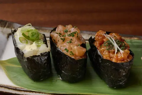 Drei Gunkan-Maki-Sushi mit Lachs, Garnelen und Fisch, garniert mit Frühlingszwiebeln und Kräutern.