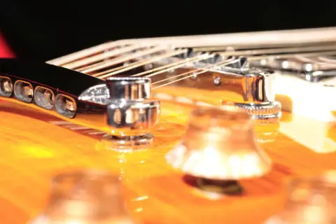 Nahaufnahme einer 12-saitigen Gitarre mit glänzenden Saiten und Chromteilen auf einem orangefarbenen Korpus.