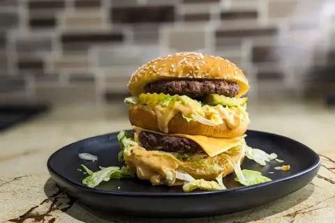 Podwójny burger z serem, sałatą i sosem na czarnym talerzu. Zastanawiasz się, ile kalorii ma Big Mac?