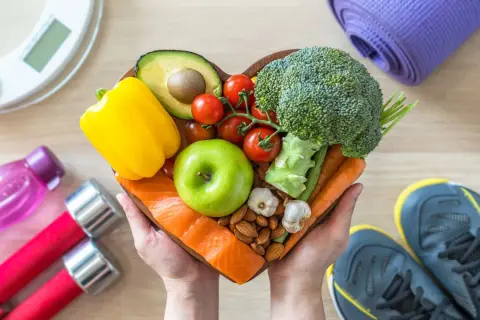 Mani che sorreggono un cuore di cibo sano: salmone, mela verde, avocado, verdure e frutta secca. Perfetto quando mangiare la mela per uno stile di vita attivo.