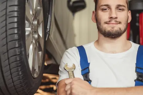 Uśmiechnięty mechanik z kluczem w dłoni, gotowy do pracy przy aucie hybrydowym. To on stoi za nowymi certyfikatami dla mechaników.