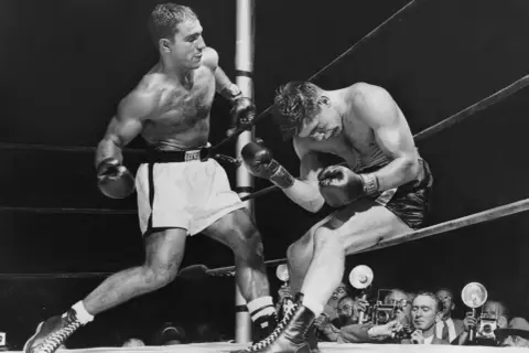 Two boxers in a ring, one on the offensive. Rocky Marciano, who won all 49 of his professional fights, is depicted here.