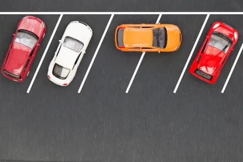 Cztery samochodziki na parkingu, gotowe do równoległego parkowania. Czerwony, biały, pomarańczowy i znów czerwony.