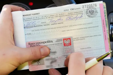 Ręka trzyma mandat karny na 300 zł, wystawiony za parkowanie na zakazie. Obok dowód osobisty.