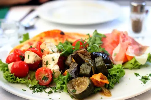 Assiette d'antipasti colorée : tomates cerises, mozzarella, légumes grillés, jambon cru et une part de pizza. Une recette d'antipasti parfaite pour l'été.
