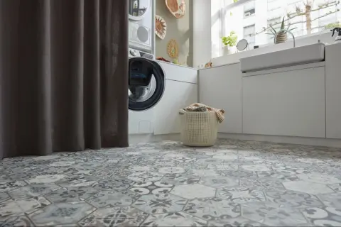 Buanderie moderne avec un sol en carrelage hexagonal aux motifs vintage. Une machine à laver et un panier à linge sont visibles.