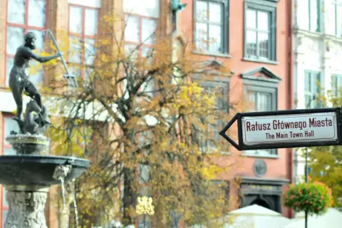 Fontanna Neptuna i drogowskaz na Ratusz Głównego Miasta w altstadt Danzig. Jesienne liście drzew tworzą tło dla zabytkowej architektury.
