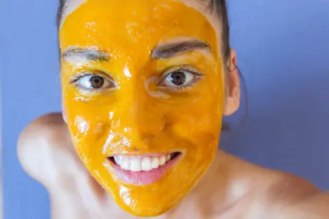 Uśmiechnięta twarz z maseczką z kurkumy, która rozjaśnia cerę. Naturalne piękno w domowym spa.