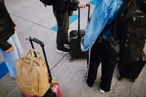 Osoby z bagażami, w tym plecak jako bagaż rejestrowany, czekają na podróż.