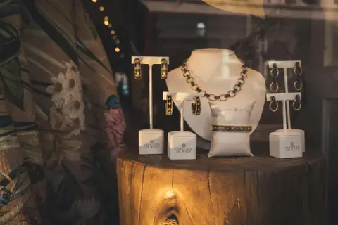 Elegancka biżuteria, w tym naszyjnik, bransoletka i kolczyki, prezentowana na drewnianym pniu. Złom złota w połączeniu z czernią tworzy luksusowy efekt.