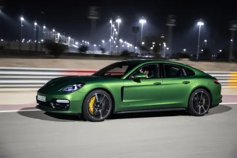 Zielony Porsche Panamera GTS pędzi nocą po torze wyścigowym, oświetlonym jaskrawymi światłami.
