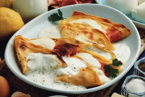 Crepes ripiene di prosciutto e formaggio, condite con una salsa cremosa. Una deliziosa panna acida ricetta per un piatto unico.