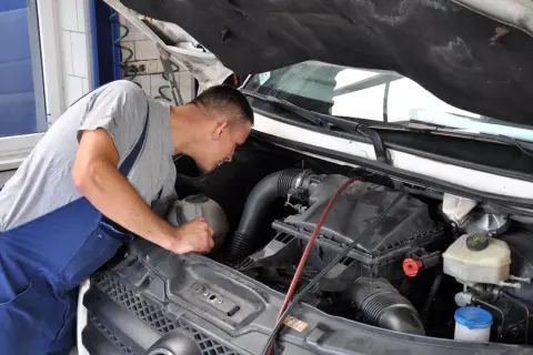 Mechanik pochyla się nad silnikiem, przygotowując się do wymiany świec żarowych.