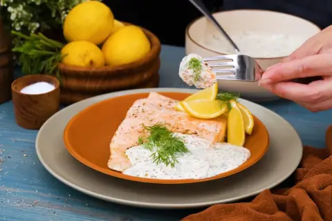 En gaffel tar en bit lax med romsås. Serverad med citron och dill.