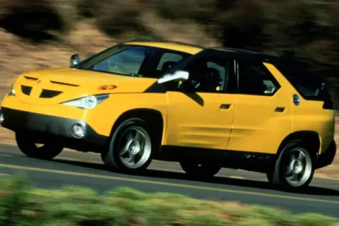 Żółty Pontiac Aztek jedzie po drodze, otoczony rozmytą zielenią i brązem.