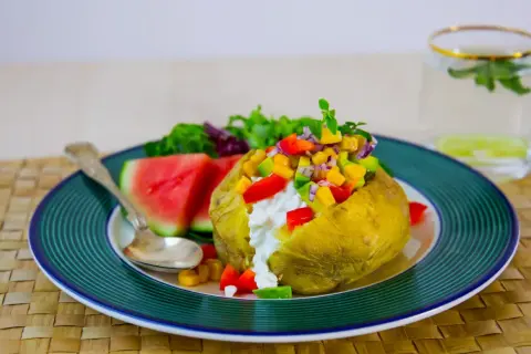 En saftig bakad potatis med en färgglad fyllning av grönsaker och en klick krämig ost. Serveras med vattenmelon och en frisk dryck.