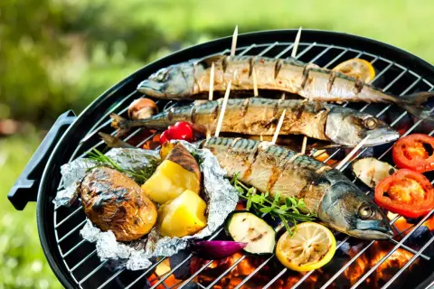 Drei ganze Makrelen werden auf einem Grill mit Kartoffeln, Tomaten und Zucchini gegrillt.