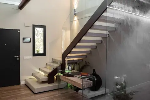 Modernas escaleras interiores prefabricadas con peldaños flotantes de hormigón y barandilla de cristal. Una cascada interior ilumina el espacio.